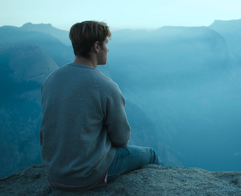 man sitting on ledge looking out at mountain